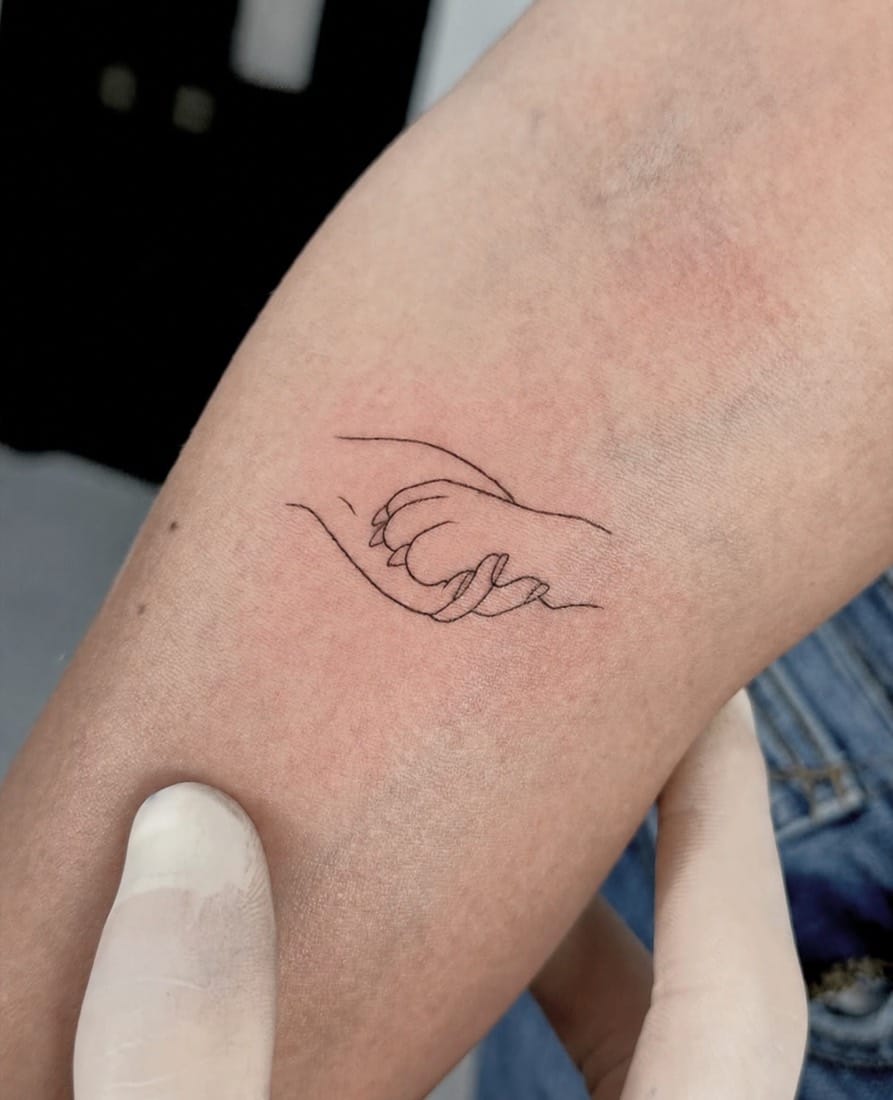 Fine line single-line tattoo of an adult and child holding hands by a Manchester Fine Line Tattoo Academy student